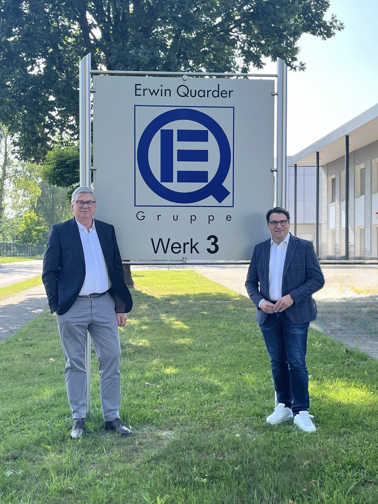 Zwei Männer in Businesskleidung vor einem "Erwin Quarder Gruppe Werk 3"-Schild.
